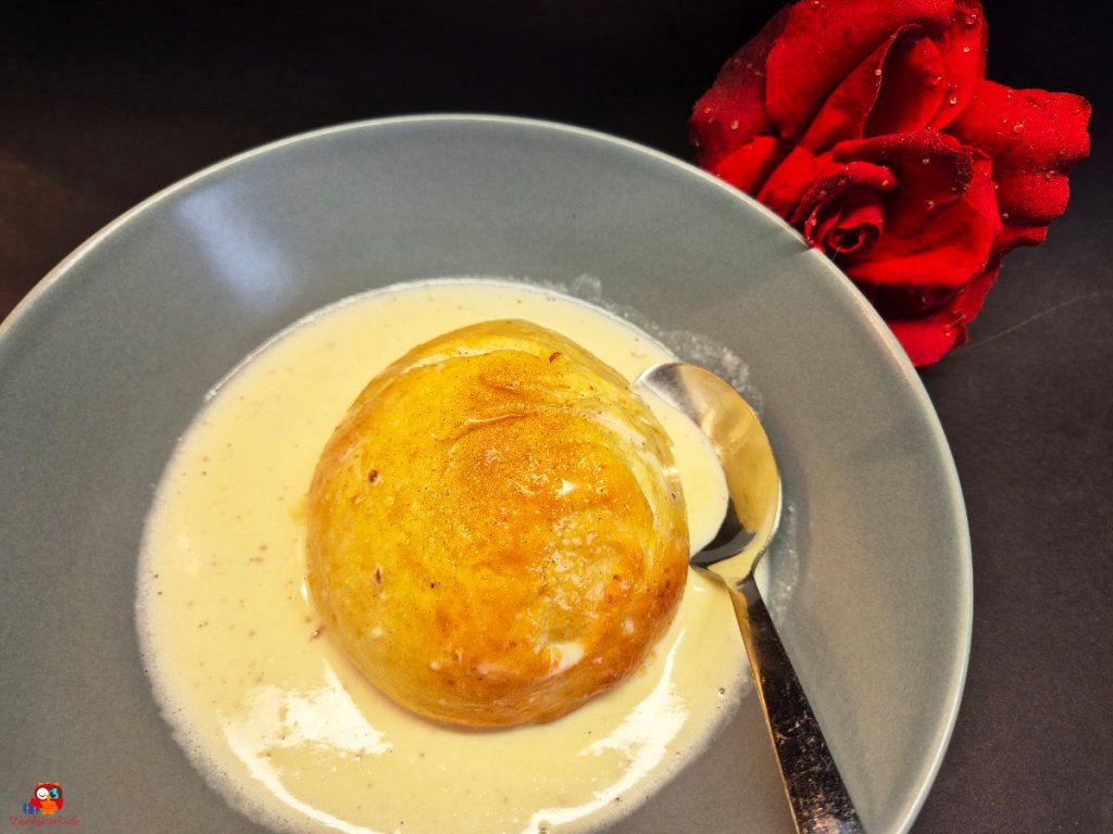 ein hefekloß, germknödel auf einem blauen teller. übergossen mit vanillesosse