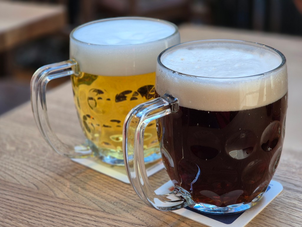 Zwei Bierkrüge, einer mit hellem Bier und der andere mit dunklem Bier, auf einem Holztisch.