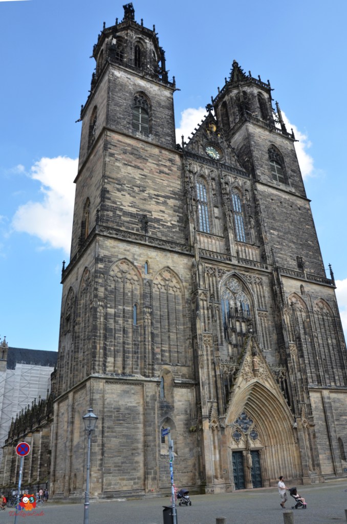 Blick auf die Fassade des Magdeburger Doms mit markanten Türmen und gotischen Elementen, unter blauem Himmel.