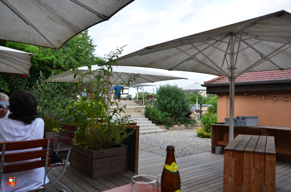 Außenbereich eines Cafés oder Restaurants in Magdeburg mit Sonnenschirmen, Tischen und Pflanzen im Vordergrund.