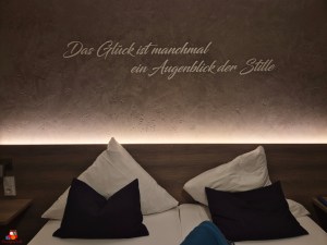 Ein Motivationsspruch an der Wand über einem Bett in einem modernen Schlafzimmer, mit Kissen in verschiedenen Farben.