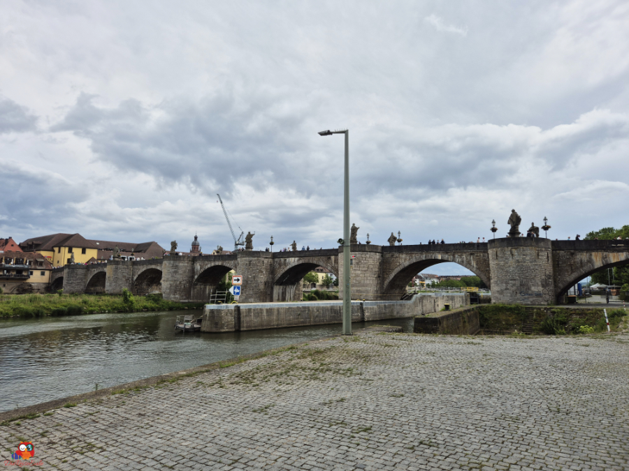 Eine historische Steinbrücke mit mehreren Bögen, umgeben von einem ruhigen Fluss, unter einem bewölkten Himmel.