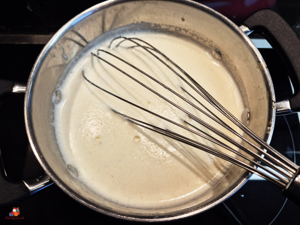 Ein Topf mit einer cremigen Sauce, in dem ein Schneebesen steht.
