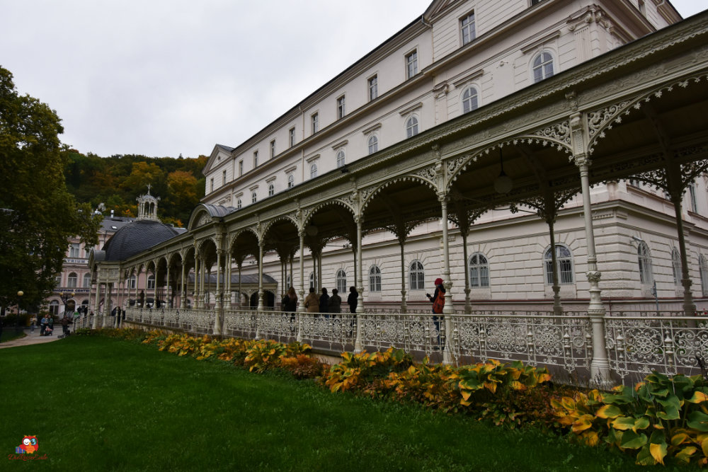 Eine elegante Veranda mit kunstvollem Geländer vor einem historischen Gebäude, umgeben von grünen Wiesen und herbstlichen Bäumen.