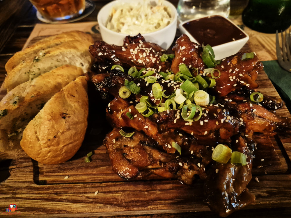 Gegrillte Rippchen mit Sesam und Frühlingszwiebeln, serviert mit einem Dip, Krautsalat und frischem Brot auf einem Holzbrett.