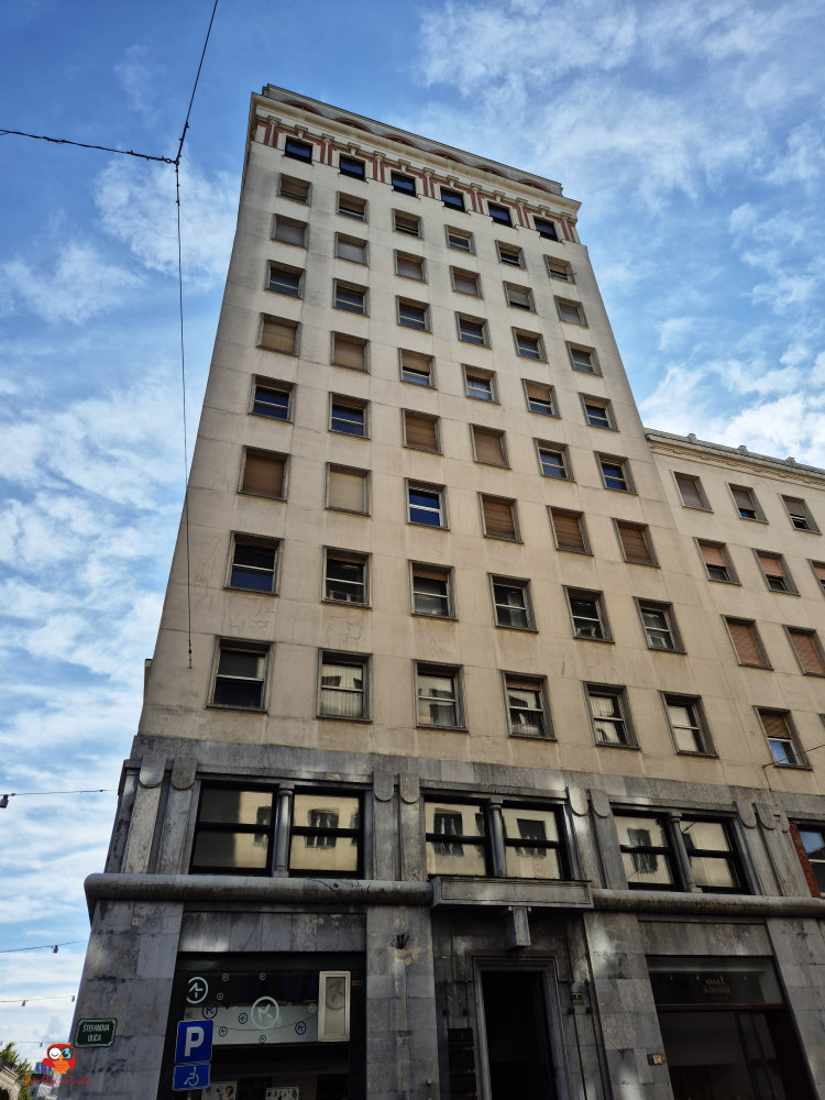 Ein hoch aufragendes Gebäude in Ljubljana mit grauer Fassade und tiefen Fenstern, unter einem klaren blauen Himmel.