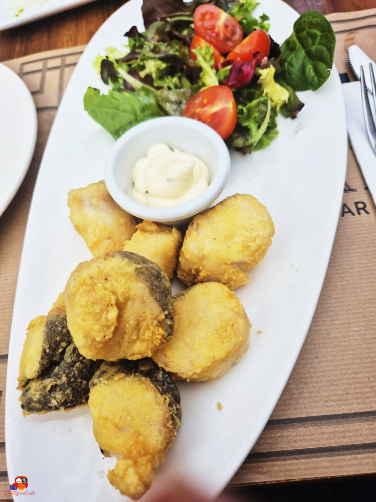 Frittierte Fischstücke serviert mit einem bunten Salat und einer Schale Mayonnaise auf einem weißen Teller.